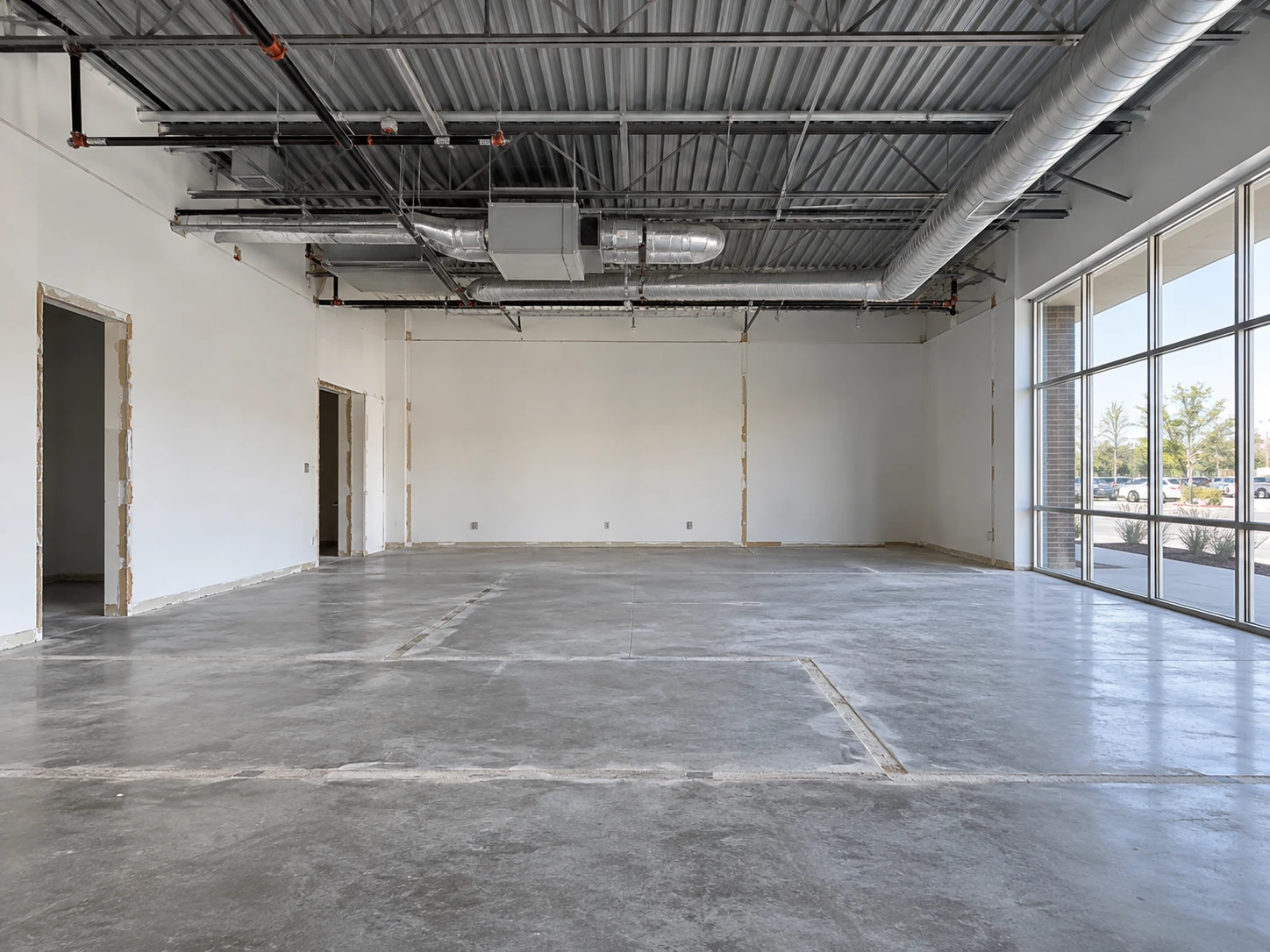 Open commercial suite with a cleared concrete floor, retained perimeter walls, and exposed overhead services