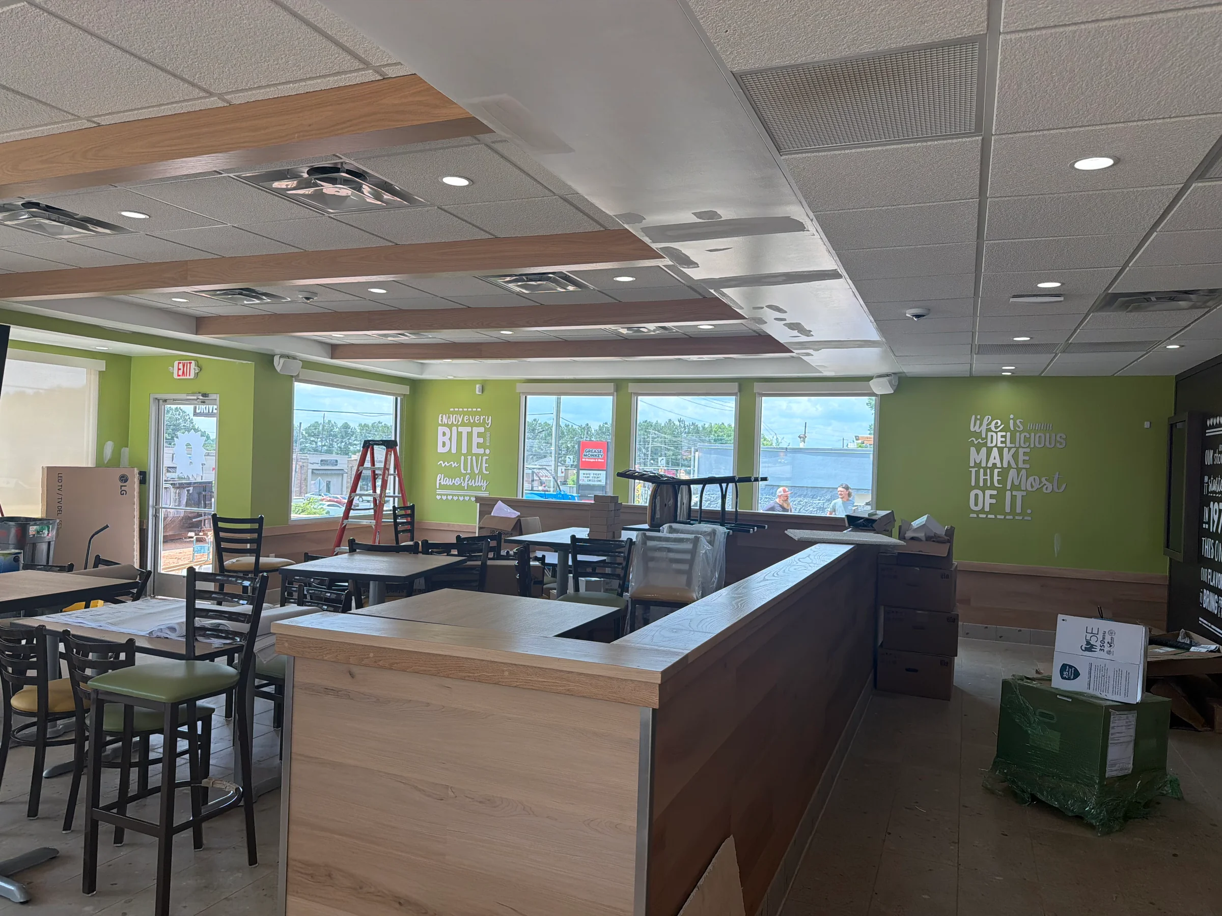 Restaurant interior during construction with green walls, ceiling details, dining furniture, and finish work in progress